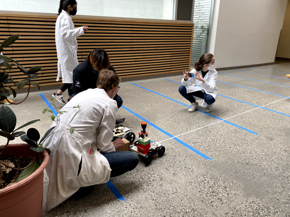 4 individuals are taking photos and measuring the distance the car travelled on the competition track